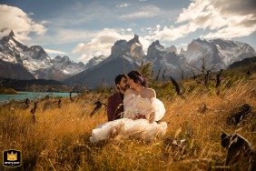 Under cloudy skies in Torres del Paine, Chile, the couple snuggles in a field with mountains behind them, sharing a quiet embrace in the open landscape together there.